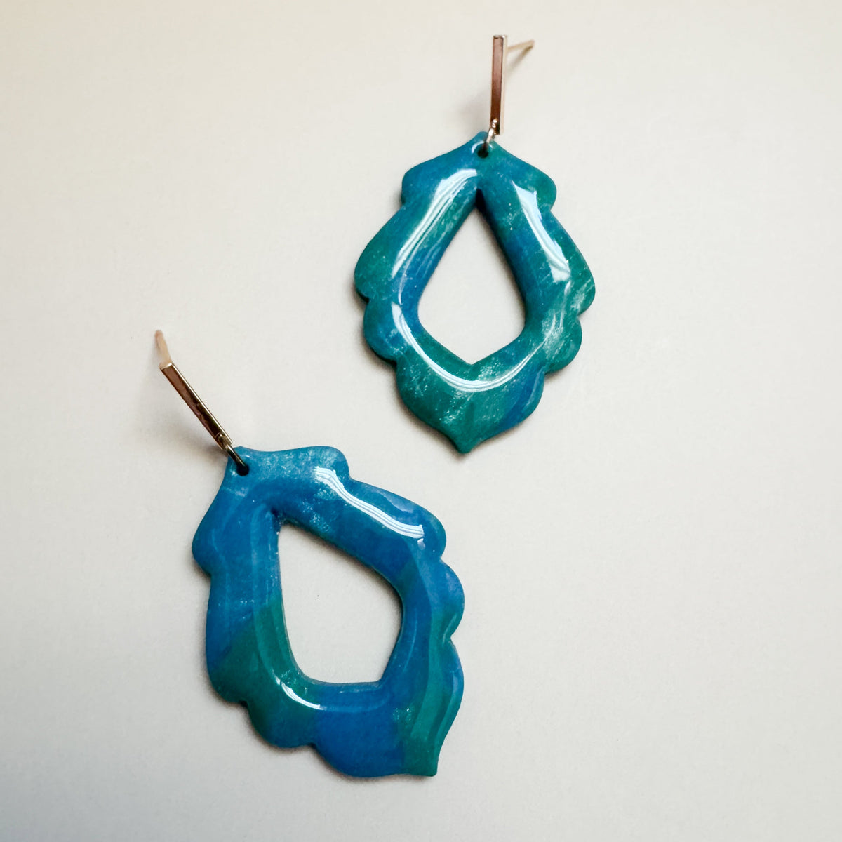 Pair of blue and green sparkling earrings on a light gray background