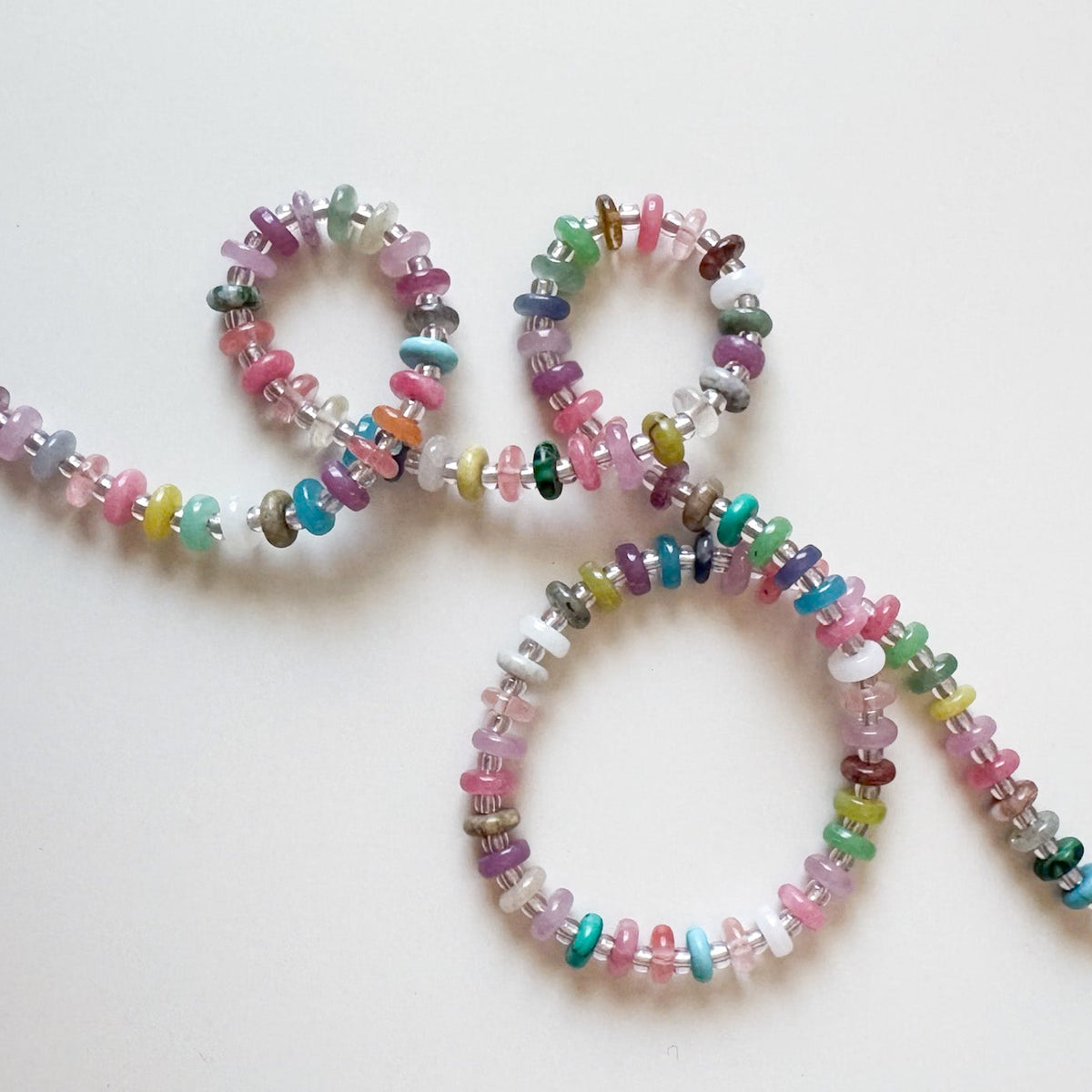 A beaded necklace made of small multicolored gemstone chips, arranged in a loop on a plain white background.