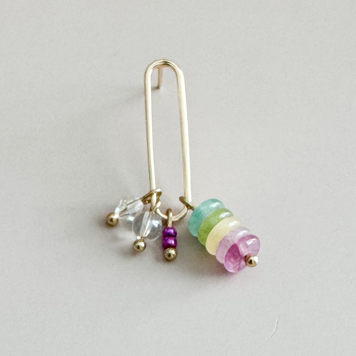 Gold earring with colorful beads on a light gray background