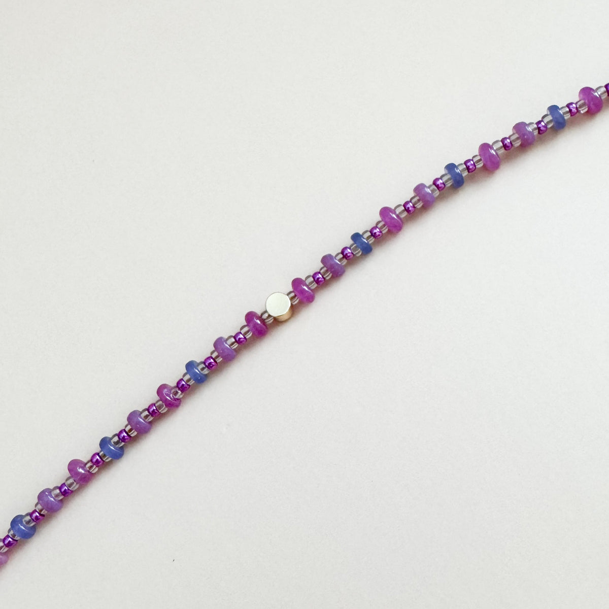 Beaded bracelet with purple and blue beads on a light gray background