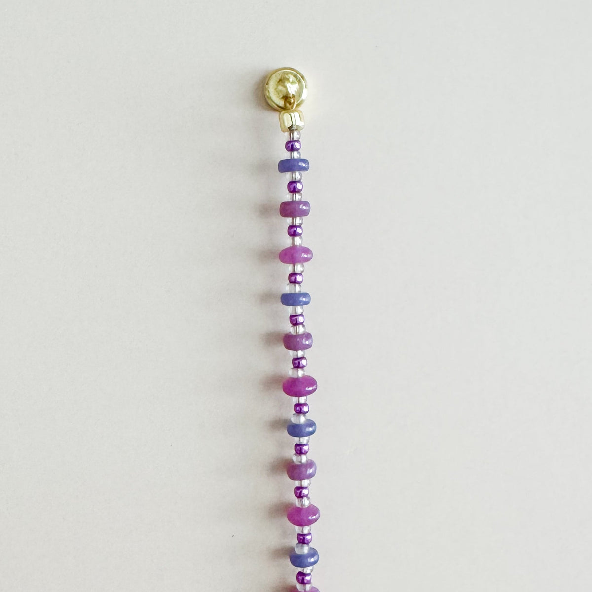 Beaded string with colorful beads and a gold clasp on a light gray background