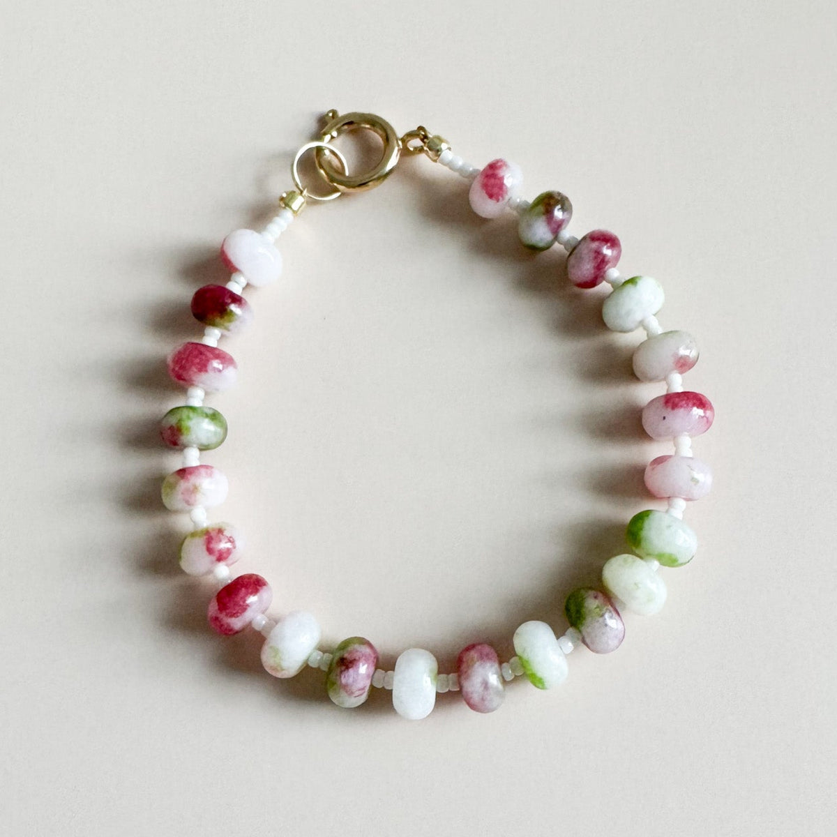 Beaded bracelet with pink, green, and white beads on a light background