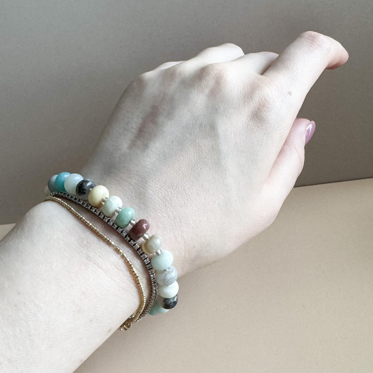 Hand wearing a bracelet with multicolored beads on a neutral background