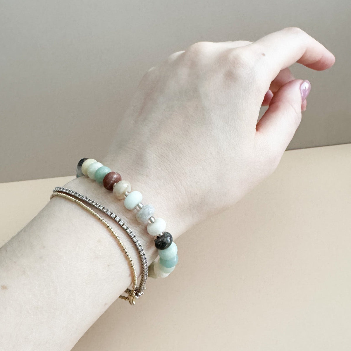 Hand wearing a bracelet with beads on a neutral background