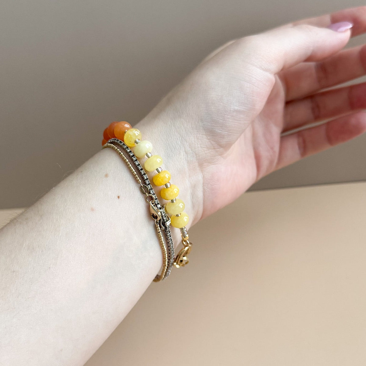 Hand wearing a bracelet with yellow beads on a neutral background