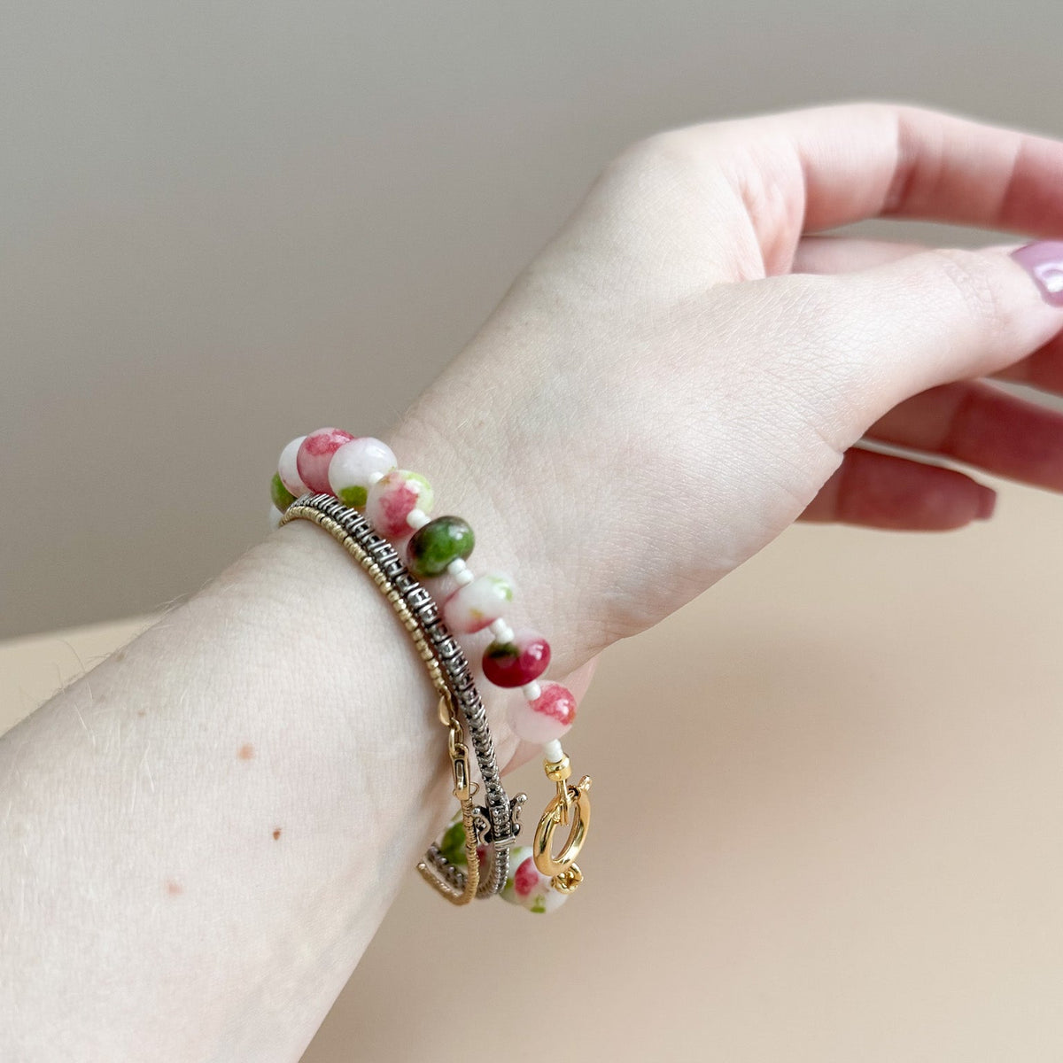 Hand wearing a bracelet with colorful beads on a neutral background