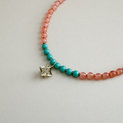 Mint green and translucent orange beaded necklace with a star-shaped charm on a light gray background