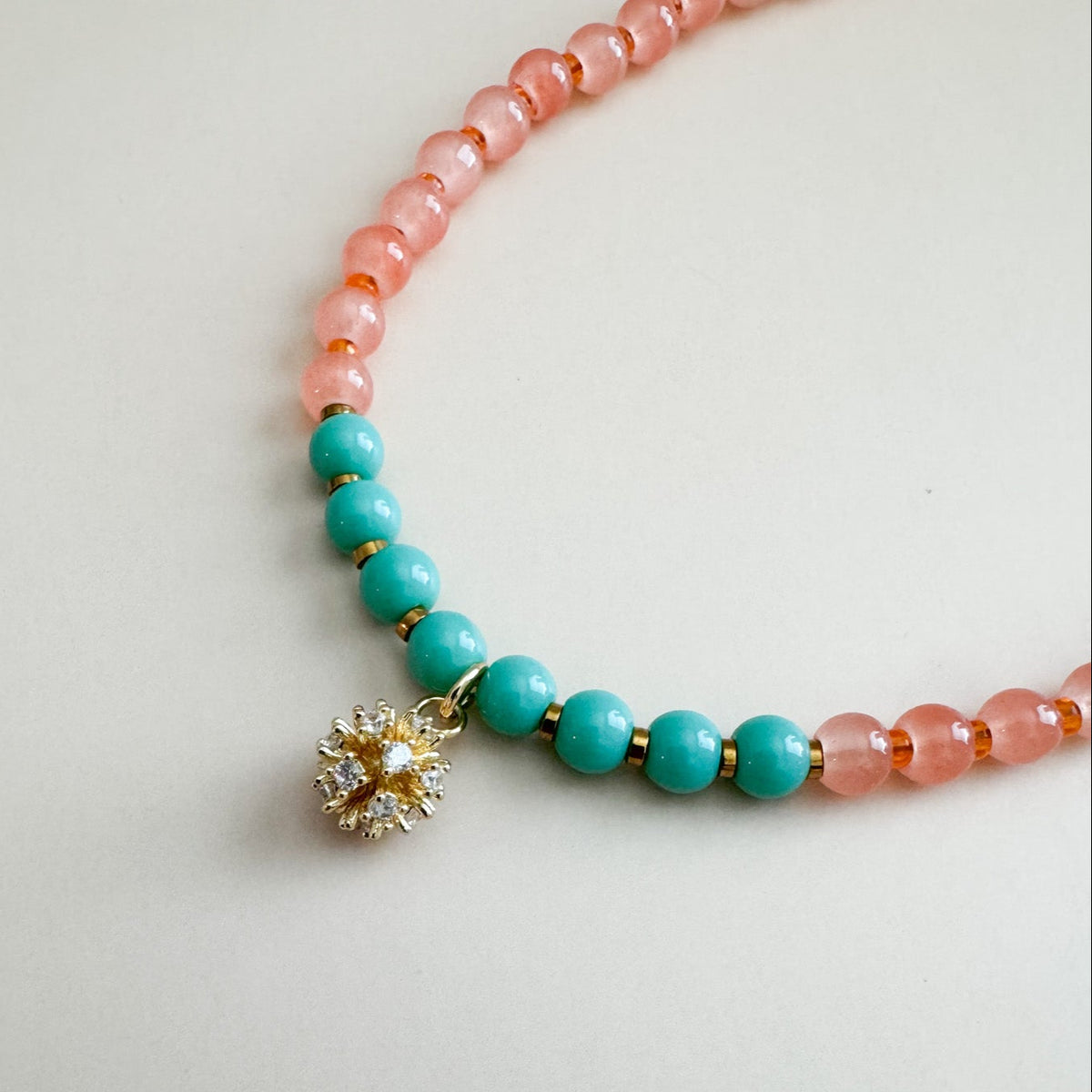 Necklace with mint green and translucent orange beads and a golden charm on a light gray background