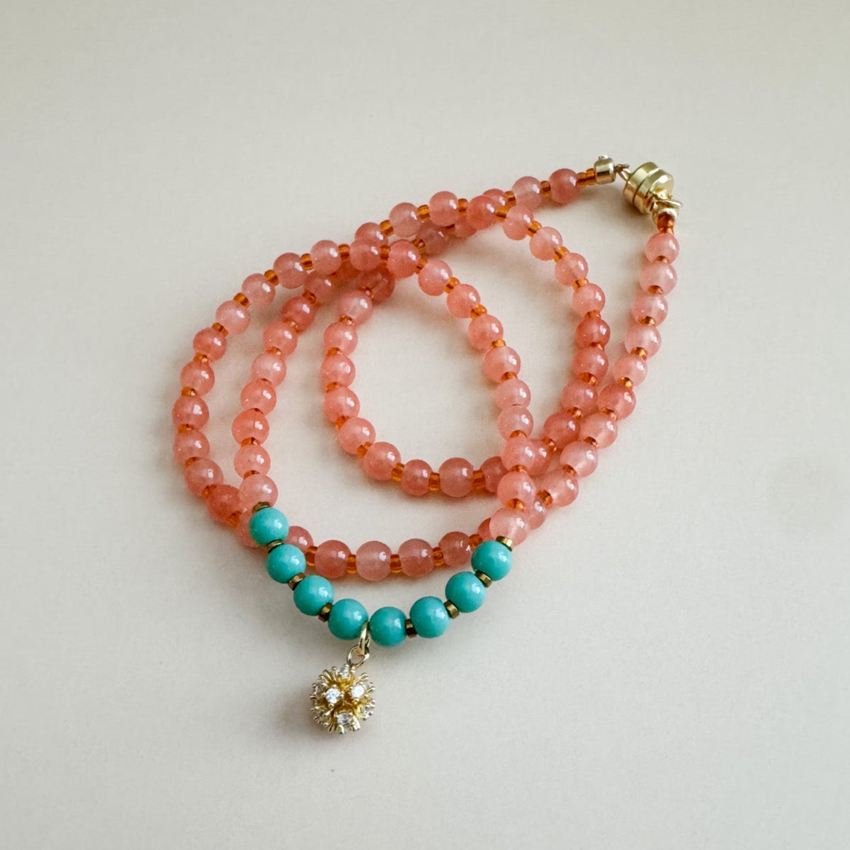 Beaded necklace with translucent orange and mint green beads on a light gray background