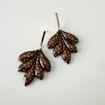 Pair of leaf-shaped earrings with brown and gold accents on a light gray background